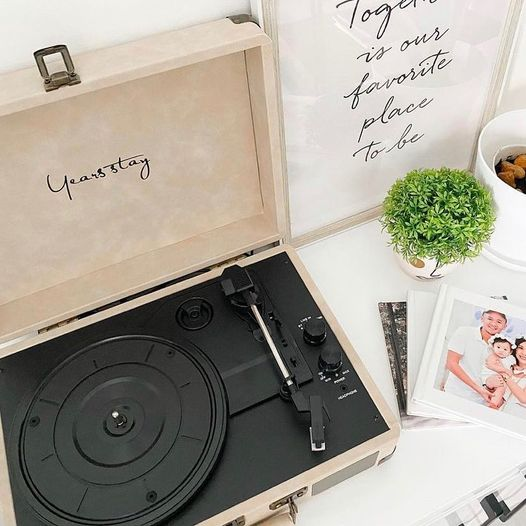 record player sitting on a table with a love note to right, and a family photo of three people hugging, next to a small free plant and a white cup